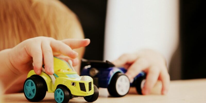 child playing with two assorted-color car plastic toys on brown wooden table